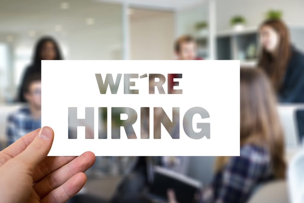 Transparent text in a white border over an office room of people which says "we're hiring"