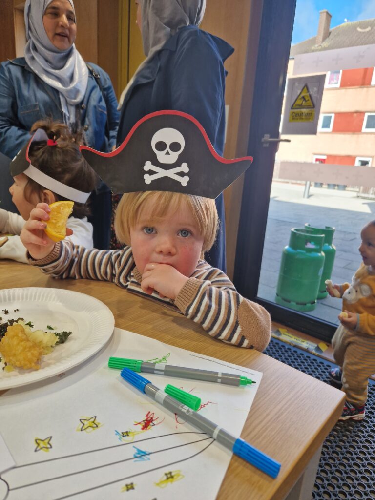 A young child wearing a pirate hat enjoying a slice of orange at our Pirate Brunch Community Meal.