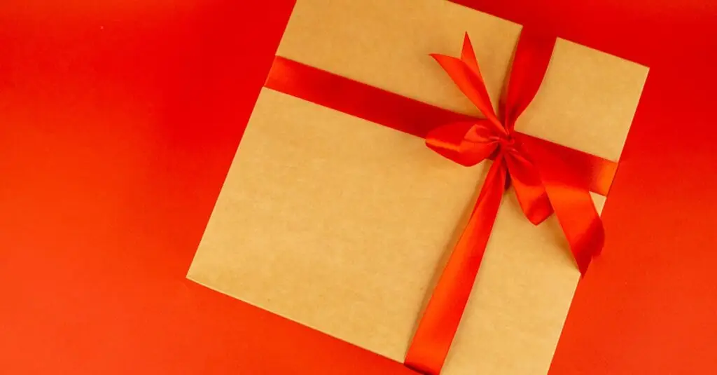 A beautifully wrapped gift box with a red ribbon on a vibrant red background, perfect for celebrations.